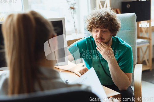 Image of Young man sitting in office during the job interview with female employee, boss or HR-manager, talking, thinking, looks confident