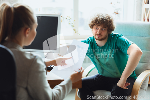 Image of Young man sitting in office during the job interview with female employee, boss or HR-manager, talking, thinking, looks confident