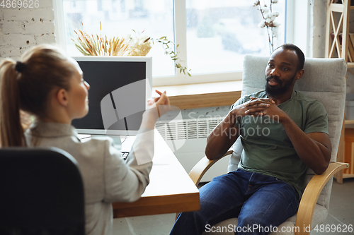 Image of Young man sitting in office during the job interview with female employee, boss or HR-manager, talking, thinking, looks confident