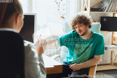 Image of Young man sitting in office during the job interview with female employee, boss or HR-manager, talking, thinking, looks confident