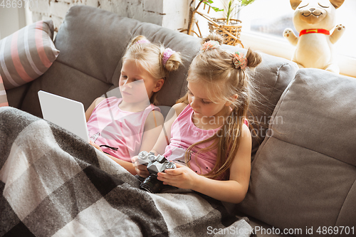 Image of Quiet little girls playing in a bedroom in cute pajamas, home style and comfort, watching cartoons, cinema, having fun