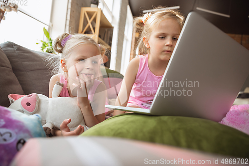 Image of Quiet little girls playing in a bedroom in cute pajamas, home style and comfort, watching cartoons, cinema, having fun