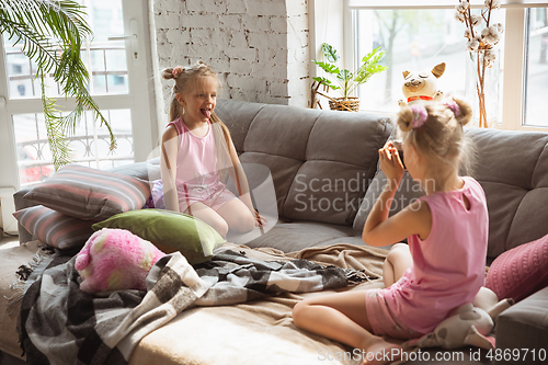 Image of Quiet little girls playing in a bedroom in cute pajamas, home style and comfort, taking a photo, having fun