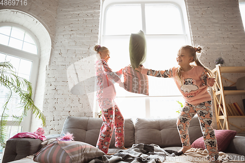 Image of Quiet little girls playing in a bedroom in cute pajamas, home style and comfort, laughting and fighting pillows