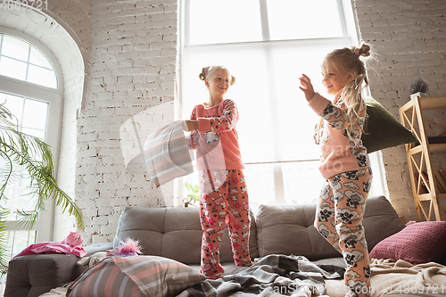 Image of Quiet little girls playing in a bedroom in cute pajamas, home style and comfort, laughting and fighting pillows