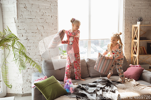 Image of Quiet little girls playing in a bedroom in cute pajamas, home style and comfort, laughting and fighting pillows