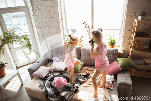 Image of Quiet little girls playing in a bedroom in cute pajamas, home style and comfort, taking a photo, having fun