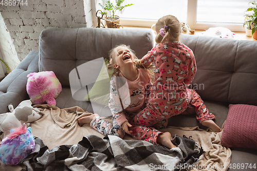 Image of Quiet little girls playing in a bedroom in cute pajamas, home style and comfort, laughting, having fun together