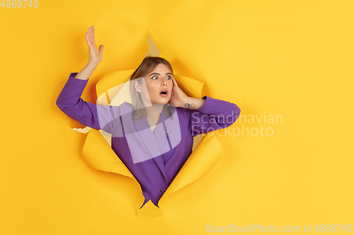 Image of Cheerful young woman poses in torn yellow paper hole background, emotional and expressive