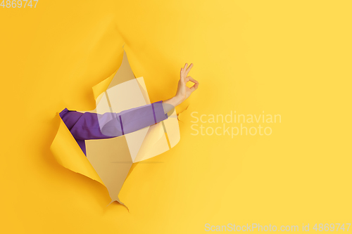 Image of Female hand gesturing in torn yellow paper hole background
