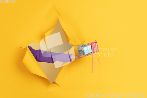 Image of Female hand giving gift in torn yellow paper hole background, celebration