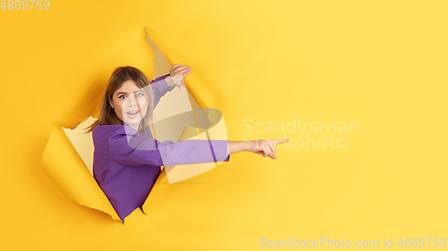 Image of Cheerful young woman poses in torn yellow paper hole background, emotional and expressive, flyer with copyspace