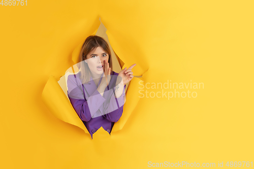 Image of Cheerful young woman poses in torn yellow paper hole background, emotional and expressive