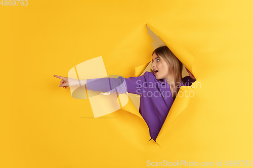 Image of Cheerful young woman poses in torn yellow paper hole background, emotional and expressive