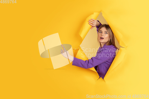 Image of Cheerful young woman poses in torn yellow paper hole background, emotional and expressive