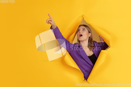 Image of Cheerful young woman poses in torn yellow paper hole background, emotional and expressive