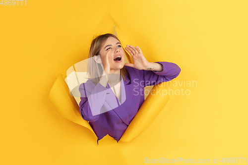 Image of Cheerful young woman poses in torn yellow paper hole background, emotional and expressive