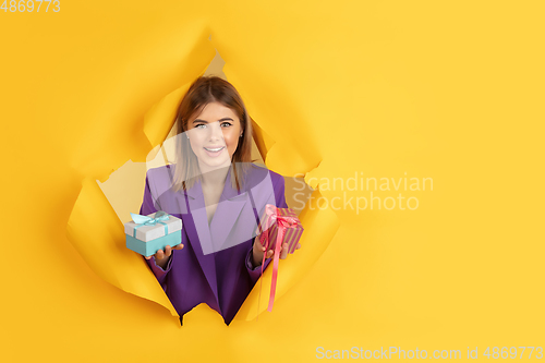 Image of Cheerful young woman poses in torn yellow paper hole background, emotional and expressive