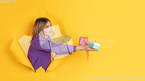 Image of Cheerful young woman poses in torn yellow paper hole background, emotional and expressive, flyer with copyspace