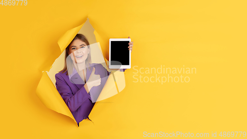 Image of Cheerful young woman poses in torn yellow paper hole background, emotional and expressive