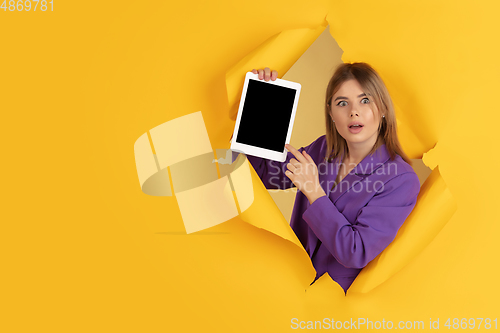 Image of Cheerful young woman poses in torn yellow paper hole background, emotional and expressive