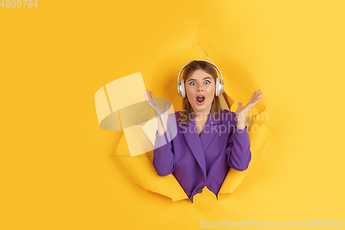 Image of Cheerful young woman poses in torn yellow paper hole background, emotional and expressive