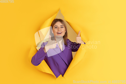 Image of Cheerful young woman poses in torn yellow paper hole background, emotional and expressive