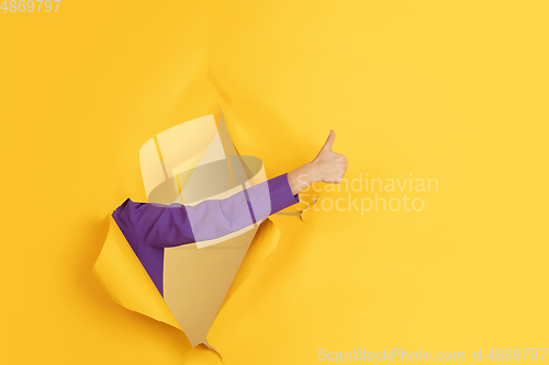 Image of Female hand gesturing in torn yellow paper hole background