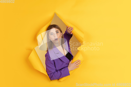 Image of Cheerful young woman poses in torn yellow paper hole background, emotional and expressive