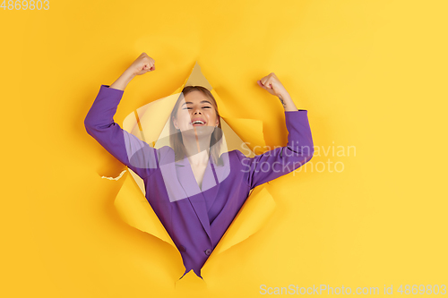 Image of Cheerful young woman poses in torn yellow paper hole background, emotional and expressive