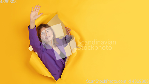 Image of Cheerful young woman poses in torn yellow paper hole background, emotional and expressive, flyer with copyspace