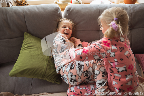 Image of Quiet little girls playing in a bedroom in cute pajamas, home style and comfort, laughting, having fun together