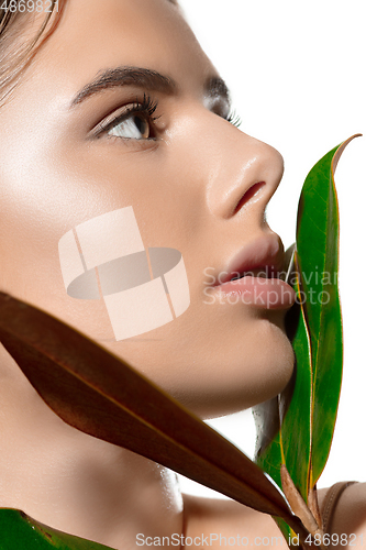 Image of Inspiration. Close up of beautiful young woman with green leaves on her face over white background. Cosmetics and makeup, natural and eco treatment, skin care