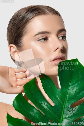 Image of Inspired. Close up of beautiful young woman with green leaves on her face over white background. Cosmetics and makeup, natural and eco treatment, skin care