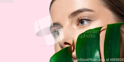 Image of Close up of beautiful young woman with green leaves on her face over white background. Cosmetics and makeup, natural and eco treatment, skin care. Flyer with copyspace.