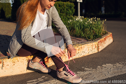 Image of Young female runner, athlete resting after jogging in the city street in sunshine. Beautiful caucasian woman training, listening to music