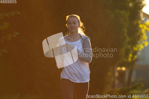 Image of Young female runner, athlete is jogging in the city street in sunshine. Beautiful caucasian woman training, listening to music