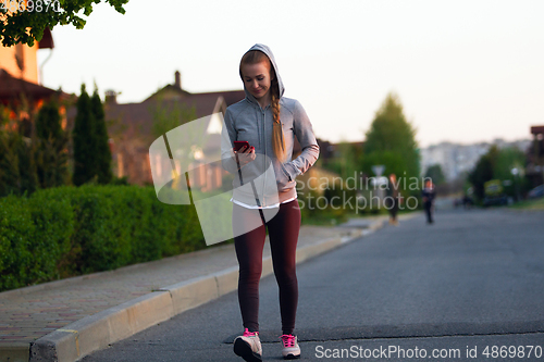 Image of Young female runner, athlete resting after jogging in the city street in sunshine. Beautiful caucasian woman training, listening to music