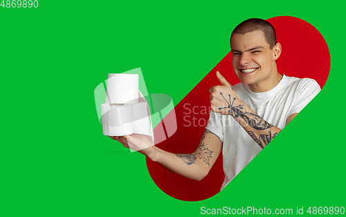 Image of Portrait of young man on bright bicolor background with geometric style, modern design, artwork. Holding toilet paper, scary smiling and thumb up