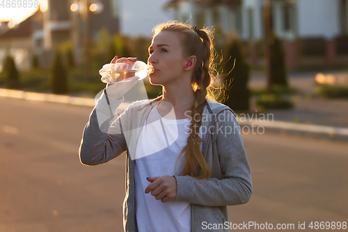 Image of Young female runner, athlete resting after jogging in the city street in sunshine. Beautiful caucasian woman training, listening to music