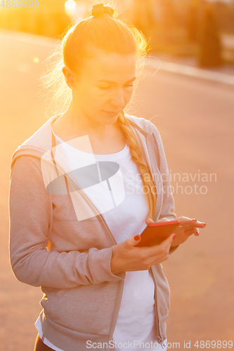 Image of Young female runner, athlete is jogging in the city street in sunshine. Beautiful caucasian woman training, listening to music