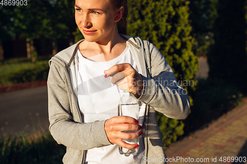 Image of Young female runner, athlete resting after jogging in the city street in sunshine. Beautiful caucasian woman training, listening to music