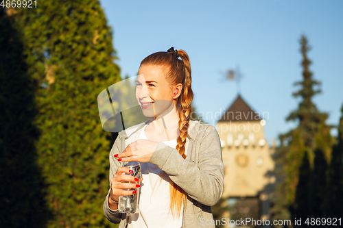 Image of Young female runner, athlete resting after jogging in the city street in sunshine. Beautiful caucasian woman training, listening to music