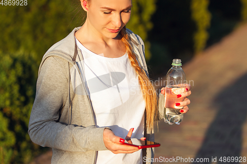 Image of Young female runner, athlete resting after jogging in the city street in sunshine. Beautiful caucasian woman training, listening to music