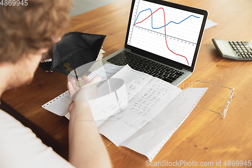 Image of Close up caucasian upset and despair man doing financial and economical reports with income graphs going down during coronavirus quarantine, problems, empty wallet