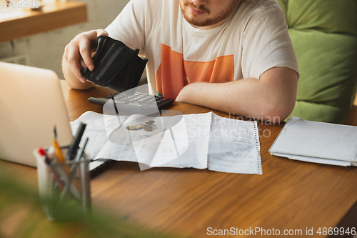 Image of Caucasian upset and despair man looking in empty wallet during coronavirus quarantine, business fall, lack of money, problems