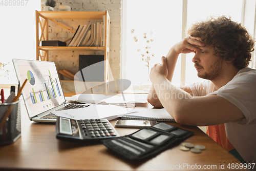 Image of Caucasian upset and despair man watching financial and economical graphs going down during coronavirus quarantine, problems