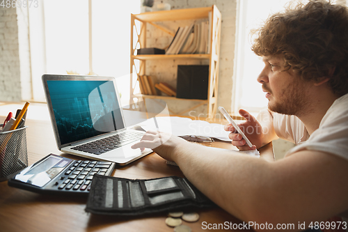 Image of Caucasian upset and despair man watching financial and economical graphs going down during coronavirus quarantine, problems