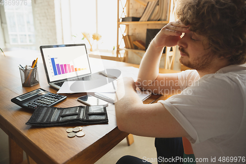 Image of Caucasian upset and despair man watching financial and economical graphs going down during coronavirus quarantine, problems