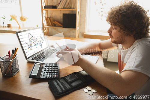 Image of Caucasian upset and despair man watching financial and economical graphs going down during coronavirus quarantine, problems